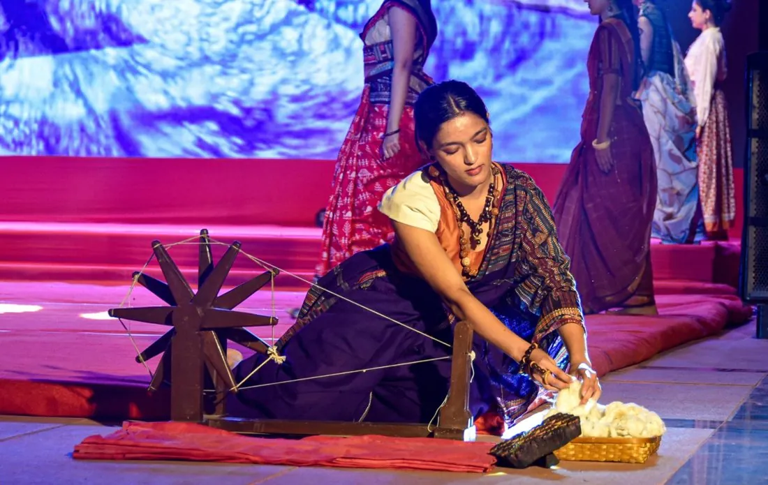 Performer spinning yarn on a charkha on stage